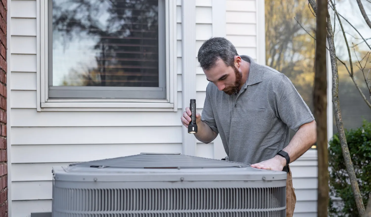 Technician inspecting an outdoor air conditioning unit with a flashlight