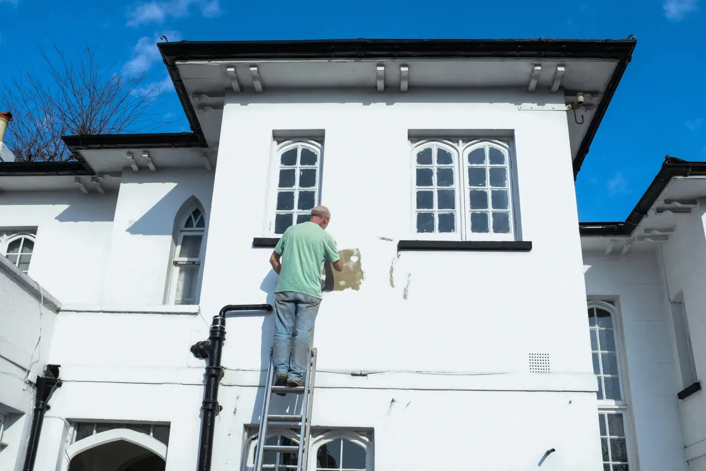 Painter on a ladder repairing a white house facade