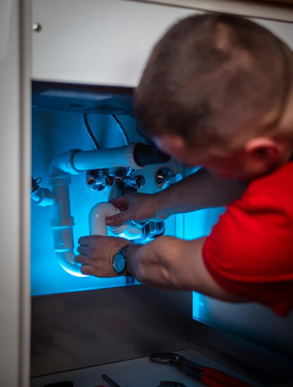 Plumber fitting a sink siphon under a counter